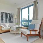 Wohnzimmer mit Sofa, Sessel, Tisch und Fenster mit blauem Rahmen.