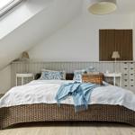 Schlafzimmer mit Dachschrägen, Wickerbett, zwei Nachttischen und Holzboden.
