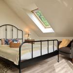 Schlafzimmer mit Dachschrägen, Bett, Sessel und Dachfenster mit Blick auf Grün.