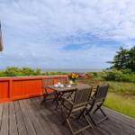 Terrasse mit Tisch und Stühlen, Blick auf Meer und grüne Landschaft.