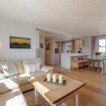 Wohn- und Essbereich mit Holzboden, Sofa, Tisch und Küchenbereich mit Meerblick.