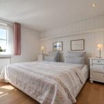 Schlafzimmer mit Doppelbett, weißen Wänden und Holzboden. Fenster mit rosa Vorhang.