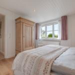 Schlafzimmer mit Bett, Holzschrank und Fenster mit Blick auf Grün.