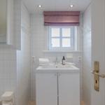 Badezimmer mit Waschbecken, Toilette und Fenster mit Rollladen.
