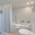 Badezimmer mit Dusche, Badewanne und Toilette. Weiße Fliesen und moderne Einrichtung.