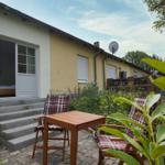Haus mit Terrasse, Tisch und Stühlen. Durchgangstür führt ins Schlafzimmer.