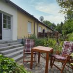 Terrasse mit Tisch und zwei Stühlen vor einem Haus mit Garten.
