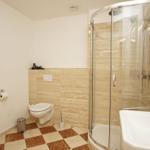 Badezimmer mit Dusche, Waschbecken und Toilette. Fliesenboden und Wandverkleidung.