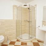 Badezimmer mit Dusche, Waschbecken und Toilette. Fliesen und Spiegel sichtbar.