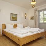 Schlafzimmer mit Holzbett, Nachttisch und Fenster. Deckenleuchte und Wandlampen.