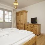 Schlafzimmer mit Holzbett, Schrank und Fernseher. Fenster mit Blick auf Garten.