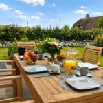 Holztisch mit Stühlen im Garten. Frühstückszubehör und Obst auf dem Tisch.