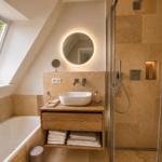 Badezimmer mit Dusche, Badewanne und Waschbecken unter Dachschrägen.