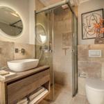 Badezimmer mit Dusche, Waschbecken und Toilette. Steinwand und Holzwaschtisch.