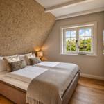 Schlafzimmer mit Doppelbett, Holzboden und Fenster mit Blick auf Bäume.