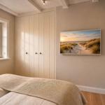 Schlafzimmer mit Bett, Kleiderschrank, Fenster und Wandbild mit Strandmotiv.
