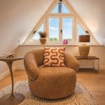 Eckzimmer mit Sessel, Tisch und Fenster mit Blick nach draußen.