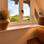 Dachfenster mit Blick auf grüne Landschaft, Pflanze im Topf und Lampe auf Tisch.