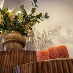 Ein brauner Vasenuntersatz mit Blumen und zwei orangefarbenen Kerzen auf einem Holztisch.