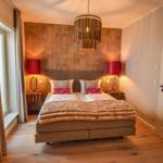 Schlafzimmer mit Bett, Nachttischen und Lampe. Holzboden und Fenster mit Vorhängen.