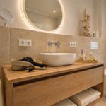 Bad mit Waschtisch, Spiegel und Toilette. Holzwaschtisch, Handtuchhalter und Fenster sichtbar.