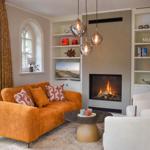 Ein Wohnzimmer mit orangefarbenem Sofa, Kamin und weißen Sesseln.