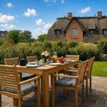 Haus mit Strohdach, Garten mit Tisch und Stühlen, Frühstückszubereitung