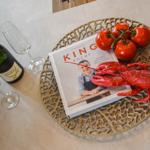 Ein Buch, eine Garnel und Tomaten auf einem Teller mit Champagnergläsern.