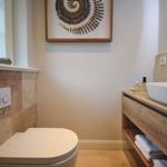 Badezimmer mit Toilette, Waschbecken und Wandbild aus Steinen.