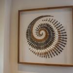 Wanddekoration aus Steinen in Form einer Spirale in einem Holzrahmen.