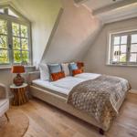 Schlafzimmer mit Doppelbett, zwei Fenstern und Holzboden.