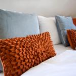 Ein Bett mit weißen Laken und Kissen in Grau und Orange.