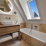 Badezimmer mit Badewanne, Waschtisch und Dusche unter Dachschrägen mit Fenster.