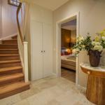 Hausflur mit Holztreppe, Schrank und Blick in Schlafzimmer mit Bett.