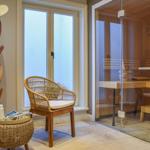 Sauna mit Glaswand, Stuhl und Hocker neben Fenster. Handtuch und Hut an Holzständer.