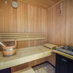 Sauna mit Holzbank, Eimer und Heizung. Wandthermometer und Holzwand.