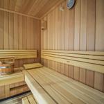 Sauna mit Holzbänken und Holzwand, Holzwaschbecken mit Besen und Thermometer an der Wand.