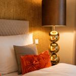 Bettkopfteil mit Kissen und einer Lampe mit goldfarbenen Kugeln.