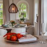 Esstisch mit Stühlen, Flasche Sekt und frischen Tomaten im Esszimmer mit Blick auf Garten.