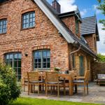 Ein Backsteinhaus mit Terrasse, Holztisch und Stühlen. Hinterhof mit Holzzaun und Grünflächen.