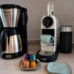Kaffeemaschine und Nespresso-System mit Tassen und Kapseln auf Arbeitsfläche.