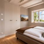 Schlafzimmer mit Bett, Kleiderschrank und Fenster mit Blick auf Grün.