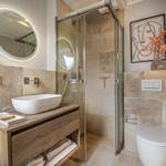 Bad mit Dusche, Waschbecken und Toilette. Steinwand und Holzschrank.