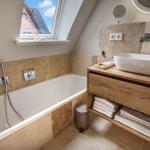 Badezimmer mit Badewanne, Waschbecken und Dusche unter Dachfenster.