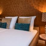 Doppelbett mit Kissen und Nachttischen mit Lampen an der Wand.