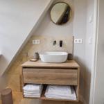 Badezimmer mit Waschtisch, Spiegel und Fenster. Handtücher und Dusche sind vorhanden.