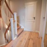 Haus mit Holztreppe, weißen Türen und Holzboden im Flur.