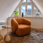 Ein Raum mit einem orangefarbenen Sessel, zwei Tischen und einem runden Teppich vor einem Dachfenster.