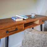 Holzschreibtisch mit zwei Schubladen und Stuhl. Darauf liegen Bücher und eine Tasse.