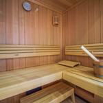 Sauna mit Holzbank, Eimer und Besen. Wandthermometer und Lüftungseinheit sichtbar.